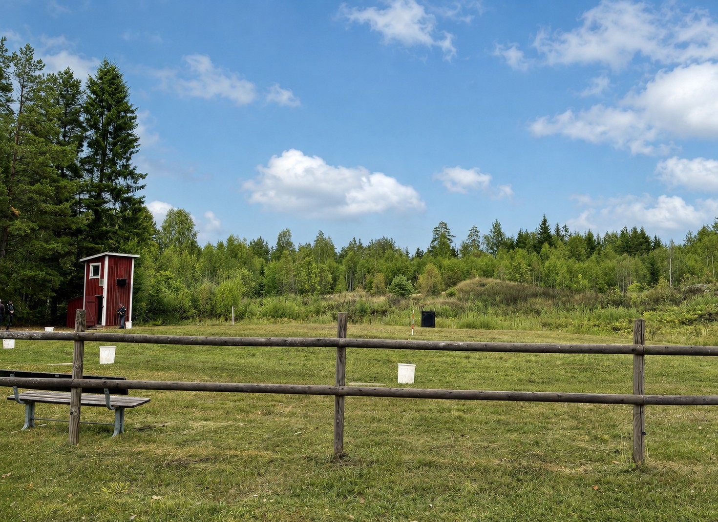 Skjutbanan i Skogstorp med skjuthytt, staket och skogsklädd kulfångsvall.